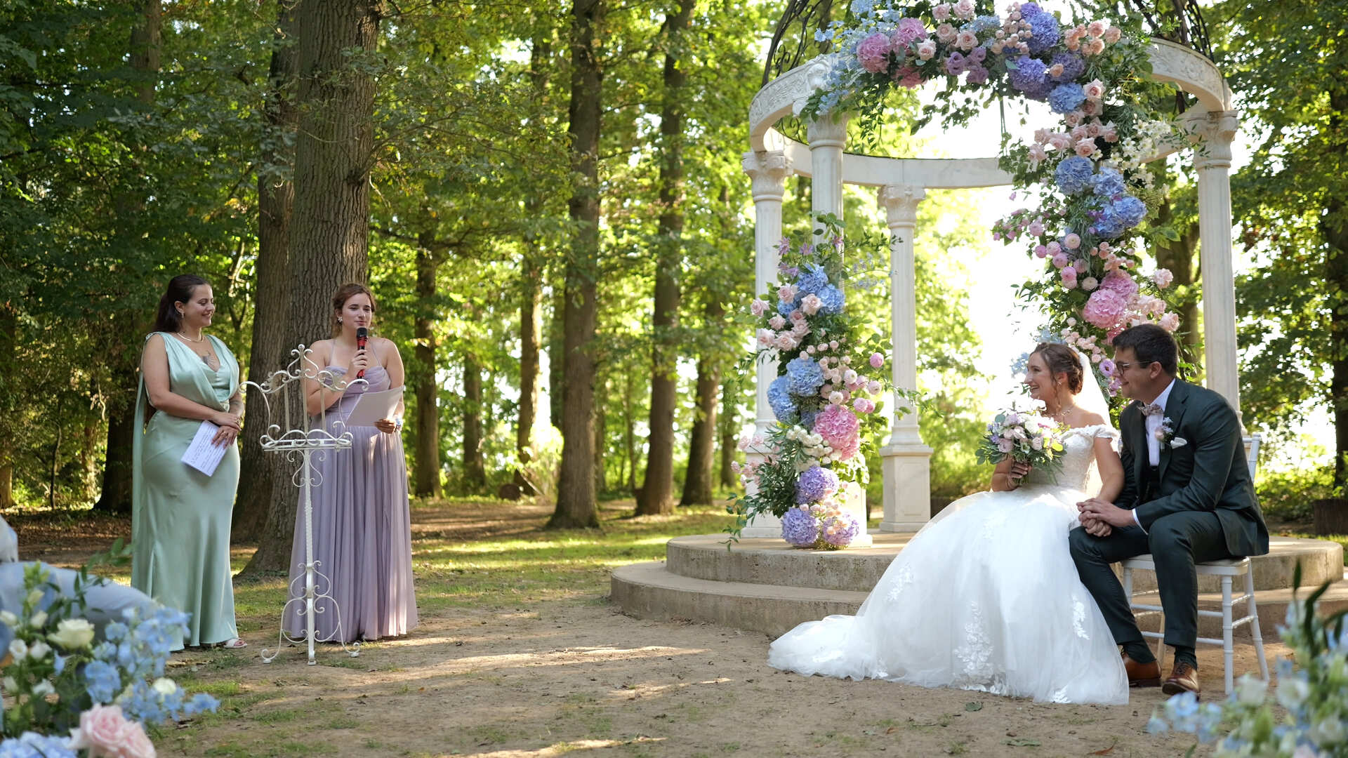 Scénographie florale romantique avec fleurs roses, parmes et bleu ciel et feuillage naturel.